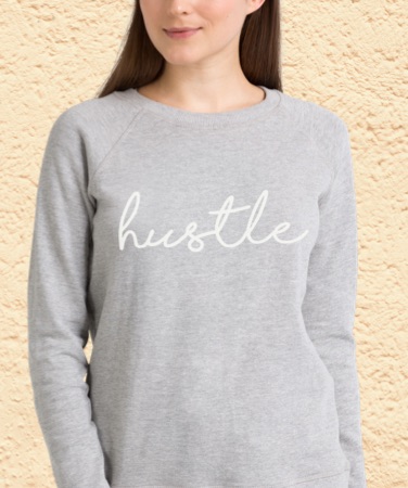 Woman wearing a grey sweatshirt with a Hustle design